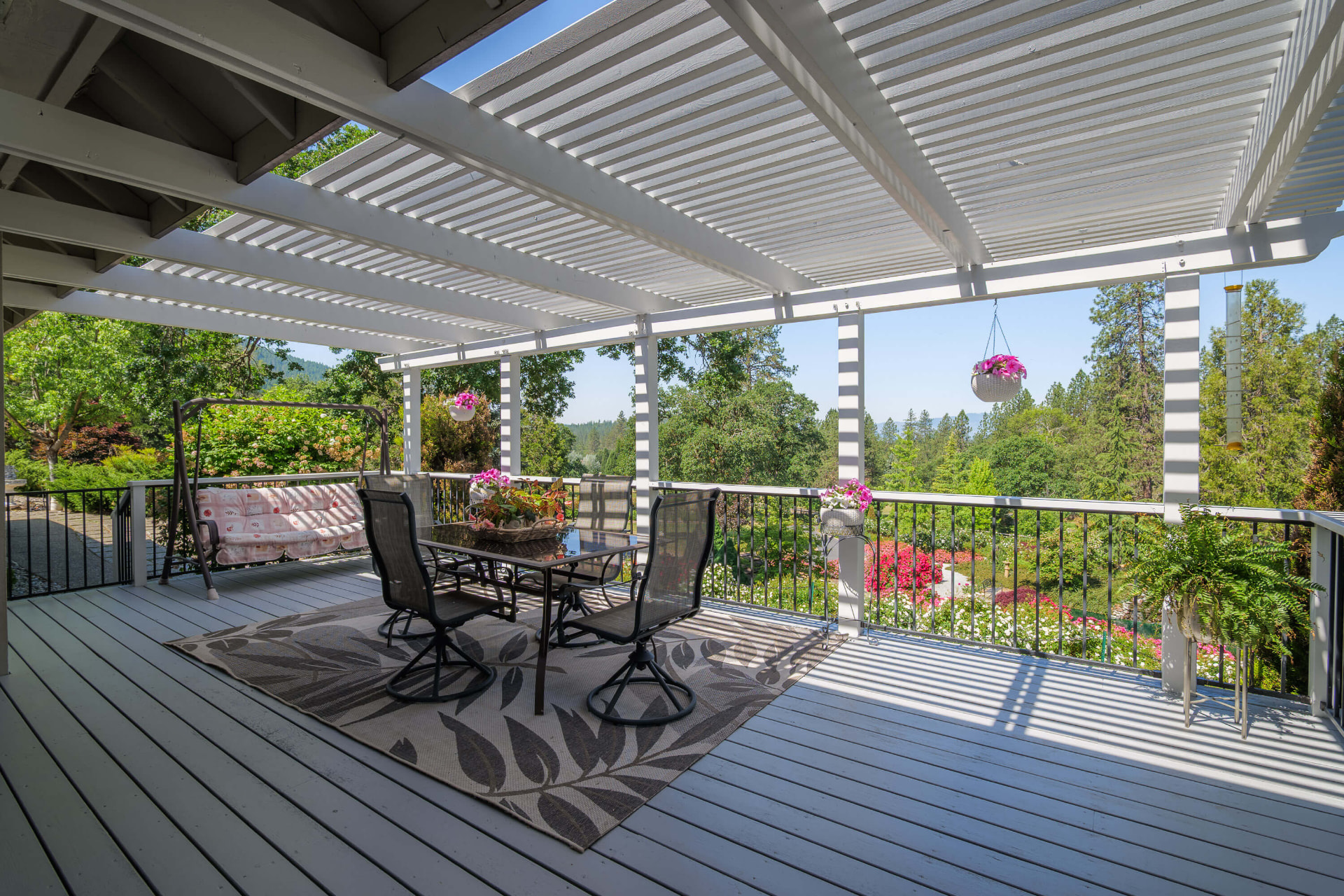 Pergola-covered deck with outdoor dining overlooking the gardens